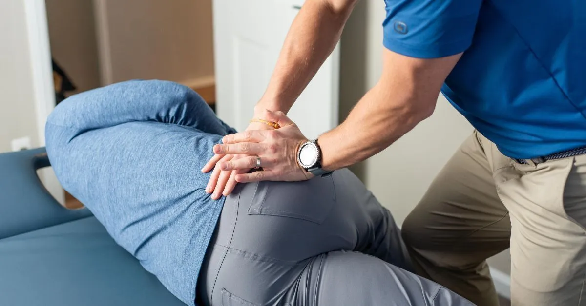 Dr. RJ Burr applying Active Release Techniques, both hands pressed into a side-lying patient's hip and glute, at REACH Rehab + Chiropractic in Plymouth, MI